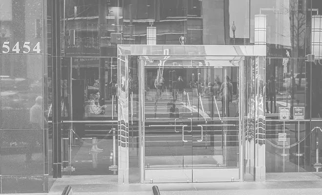 The glass entrance of the Barlow Building at 5454 Wisconsin Avenue, in black and white.