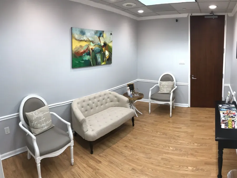 The waiting room at Bethesda Chevy Chase Advanced Dentistry, with upholstered chairs, a tufted settee and colourful art.
